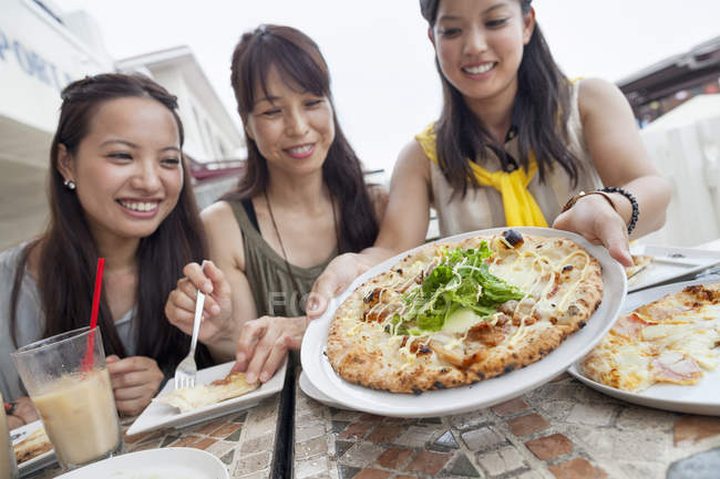 Drei fröhliche asiatische Frauen essen Pizza im Straßencafé. — Stockfoto