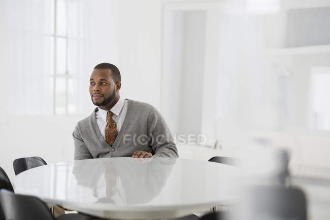 Чоловік у сорочці та краватці сидить за скляним круглим столом в офісі . — стокове фото