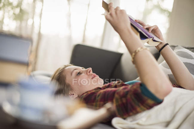 Junge Frau liegt auf Sofa und liest Buch. — Stockfoto
