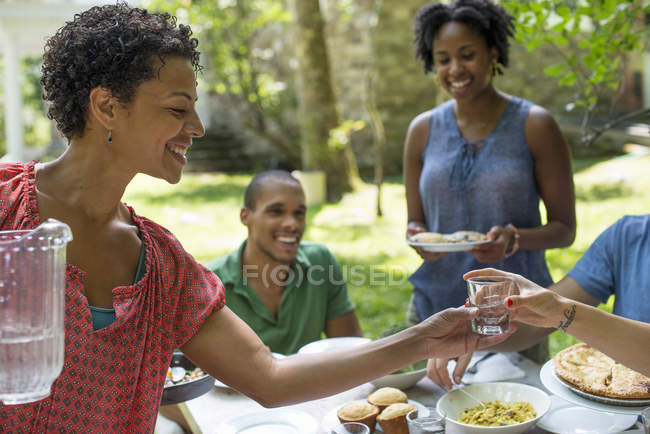Amigos y familiares se reúnen alrededor de la mesa en el jardín rural . - foto de stock