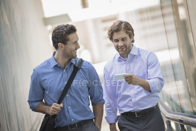 Deux hommes d'affaires marchant dans la rue urbaine et utilisant un smartphone . — Photo de stock
