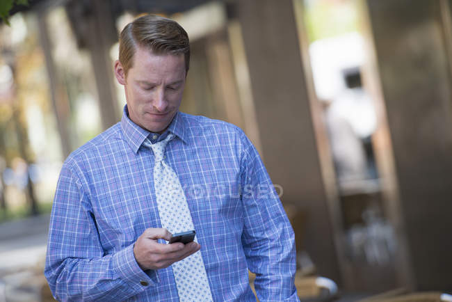Hombre adulto medio usando teléfono inteligente en la calle de la ciudad . - foto de stock