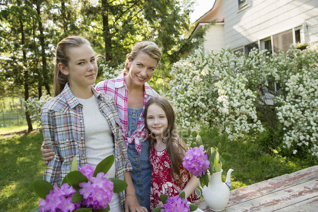 Mature woman with teenager and elementary age daughters standing in garden with flowers. — Stock Photo