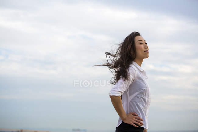 Длинноволосая женщина наслаждается бризом на открытом воздухе на фоне облачного неба
. — стоковое фото