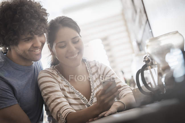 Couple looking at smartphone screen in sunlight at kitchen. — Stock Photo