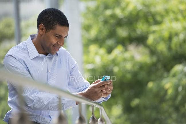 Людина, спершись на перила в парку і перевірка смартфон. — стокове фото