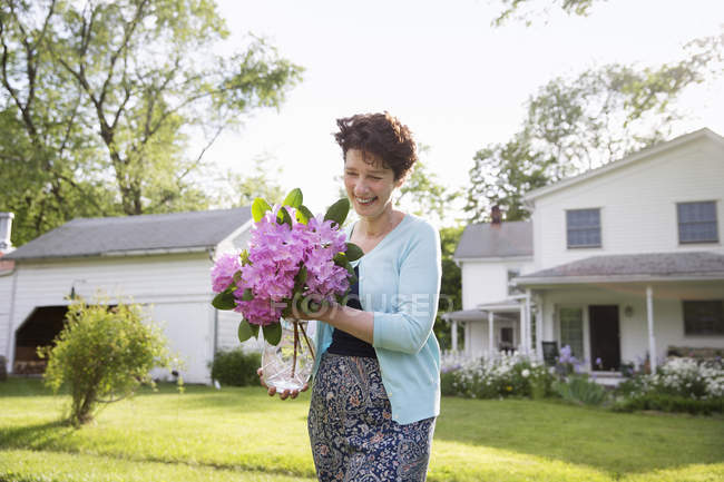 Woman carrying bunch of rhododendron flowers and smiling in garden. — Stock Photo