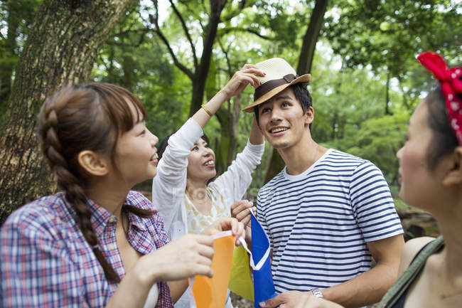 Group of young women putting straw hat on man in forest. — Stock Photo