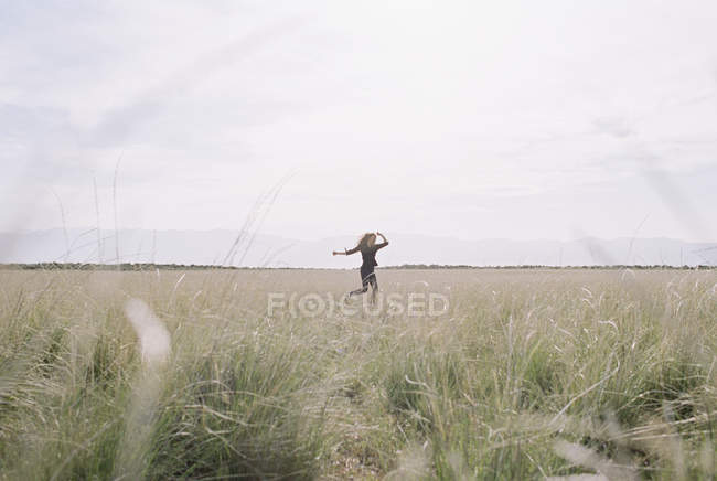 Mulher correndo através de grama longa em pastagens . — Fotografia de Stock