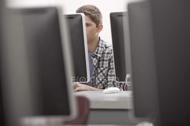 Vorpubertärer Junge arbeitet im Computerlabor mit Reihen von Computermonitoren. — Stockfoto