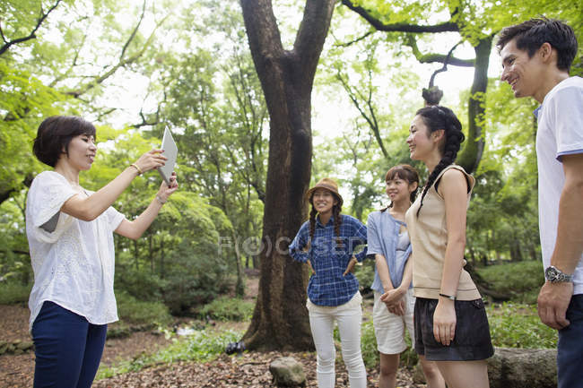 Mid adult woman taking picture with digital tablet of friends in forest. — Stock Photo