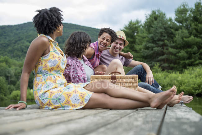 Pequeno grupo de pessoas sentadas no cais de madeira com vista para o lago rural . — Fotografia de Stock