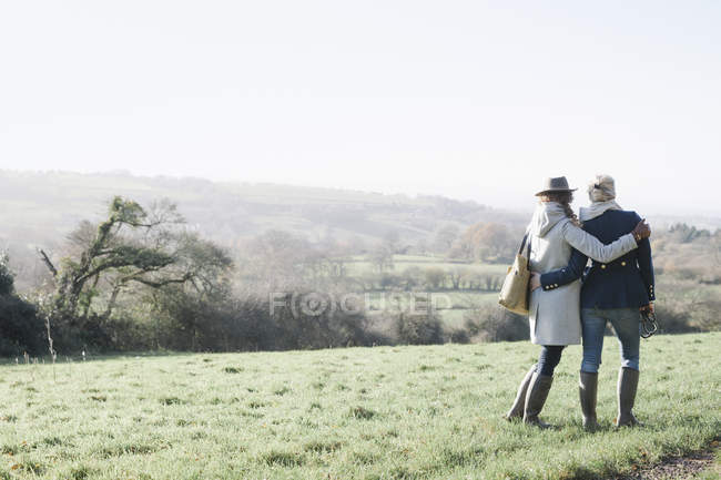 Due donne che stanno fianco a fianco e si abbracciano sul pendio erboso che domina il paesaggio del Dorset, Inghilterra . — Foto stock