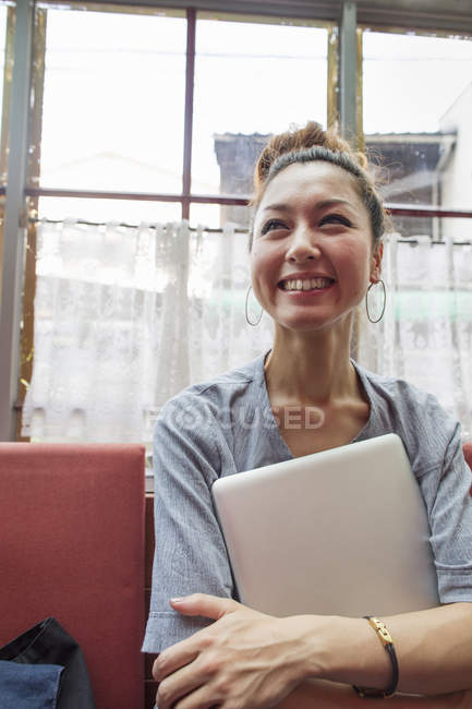 Mitte erwachsene Frau hält Laptop in der Hand und lächelt drinnen. — Stockfoto
