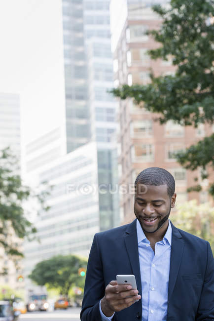 Uomo d'affari in giacca blu con smartphone sulla strada della città
. — Foto stock