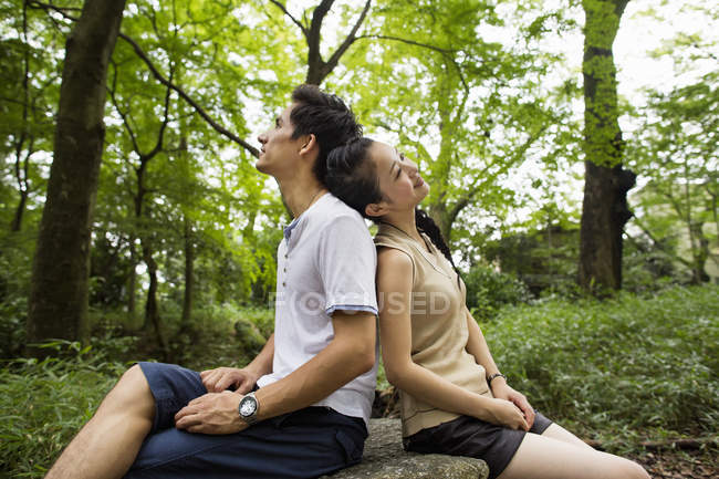 Young woman leaning on man shoulder and looking up while sitting in forest. — Stock Photo
