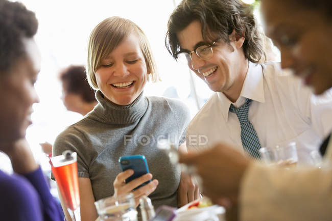 Мужчина и женщина делятся смартфоном за столом ресторана с друзьями . — стоковое фото