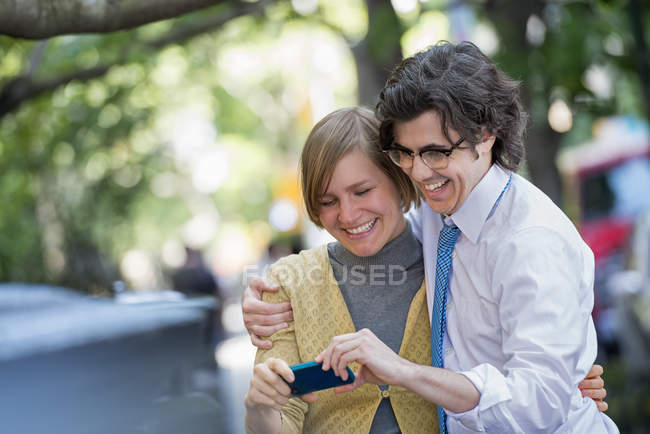 Hombre y mujer adultos compartiendo teléfono inteligente en la calle de la ciudad . - foto de stock