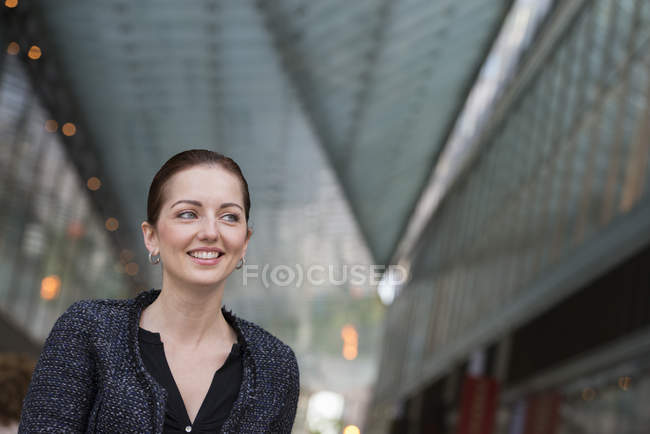 Femme adulte moyenne veste grise avec les cheveux vers le haut souriant et détournant les yeux . — Photo de stock