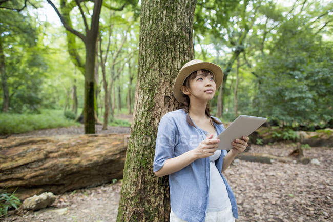Young woman holding digital tablet in sunny forest. — Stock Photo