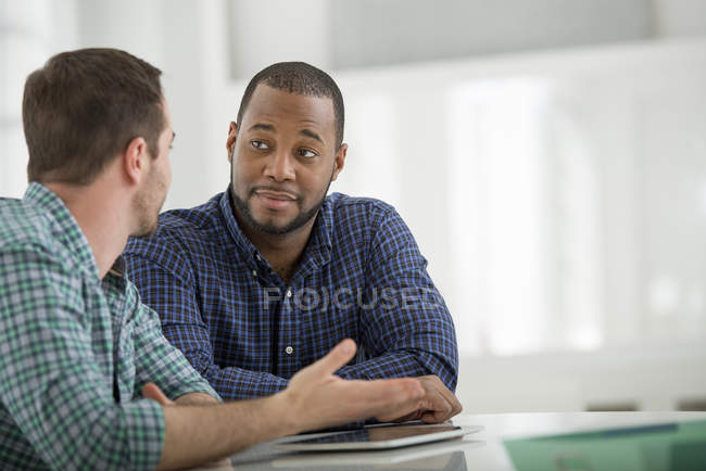 Dois homens sentados à mesa com tablet digital e conversando no escritório . — Fotografia de Stock