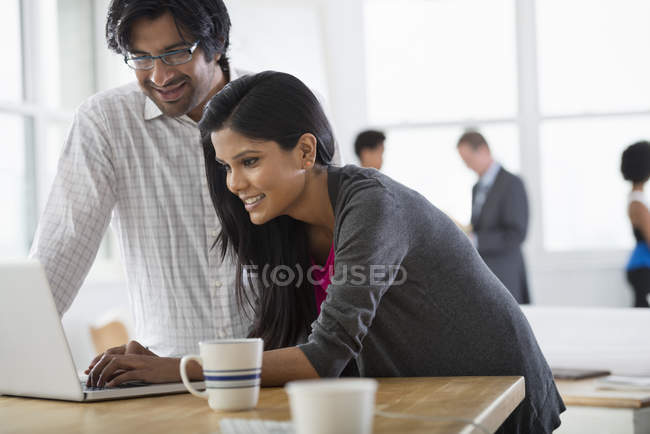 Mature man and young woman using laptop at desk with cup of coffee. — Stock Photo