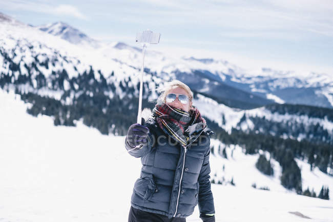 Mujer en ropa de invierno en la pista de esquí con palo seflie y teléfono inteligente . - foto de stock