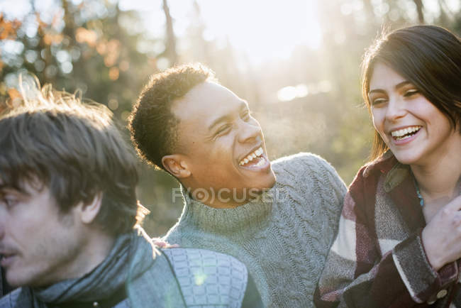 Young friends standing in sunlit forest and laughing in autumn. — Stock Photo