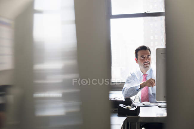 Бизнесмен в рубашке и галстуке сидит за столом и смотрит на монитор компьютера . — стоковое фото