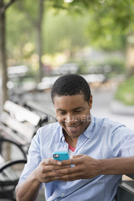 Mann sitzt auf Bank in der Stadt und benutzt Smartphone. — Stockfoto