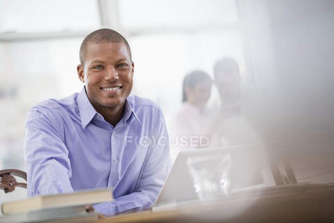 Hombre joven en camisa azul sentado en el escritorio con el ordenador portátil en la oficina . - foto de stock