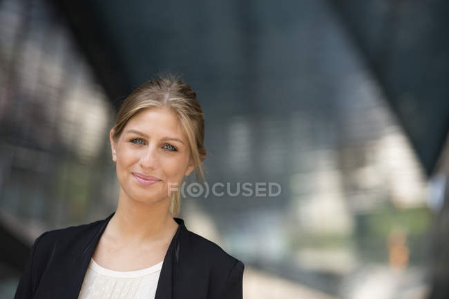 Молода бізнес-леді в чорній куртці дивиться в камеру в місті — стокове фото