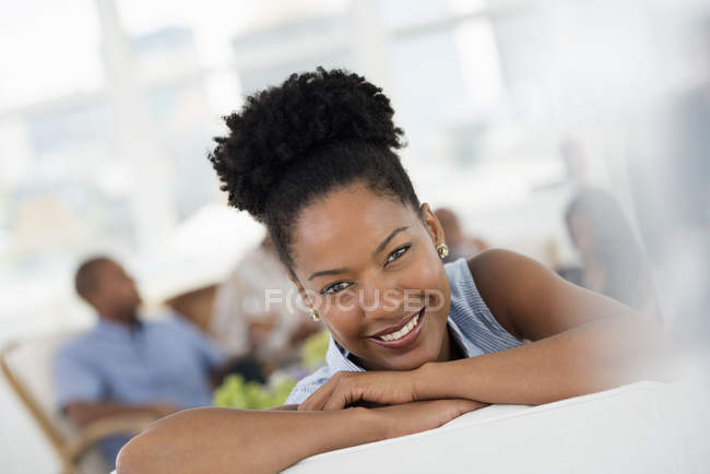 Mujer sonriendo y mirando en la cámara en la fiesta con la gente en el fondo
. - foto de stock