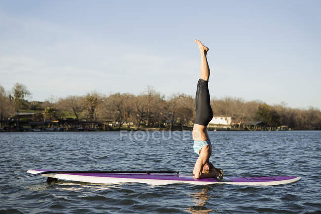 Woman doing headstand on paddle board on lake. — Stock Photo