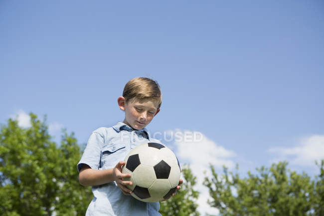 Elementary age boy holding soccer ball in park, low angle view. — Stock Photo