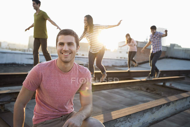 Homem sentado na frente do grupo de pessoas ao anoitecer equilibrando e andando ao longo de bicos de aço no telhado . — Fotografia de Stock
