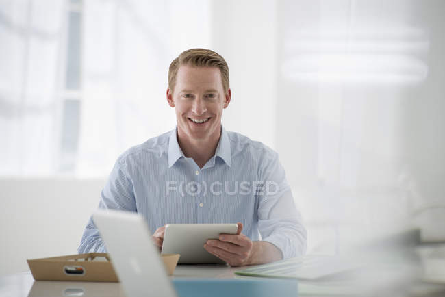 Homme d'affaires souriant et tenant tablette numérique dans un environnement de bureau aéré . — Photo de stock