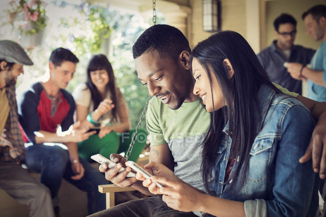 Homem e mulher verificando smartphones com amigos na festa em casa . — Fotografia de Stock