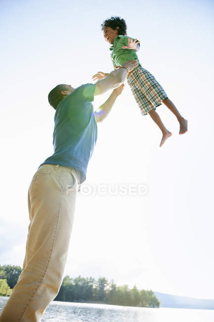 Blick auf den Vater beim Spielen und Heben des Jungen im Grundschulalter im Freien. — Stockfoto