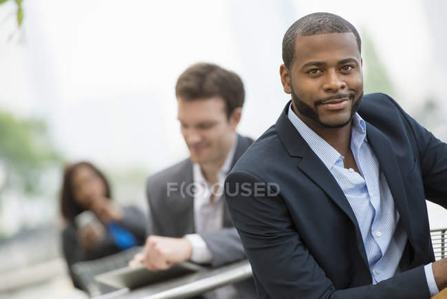 Businessman leaning on railing and looking in camera with colleagues on city street. — Stock Photo