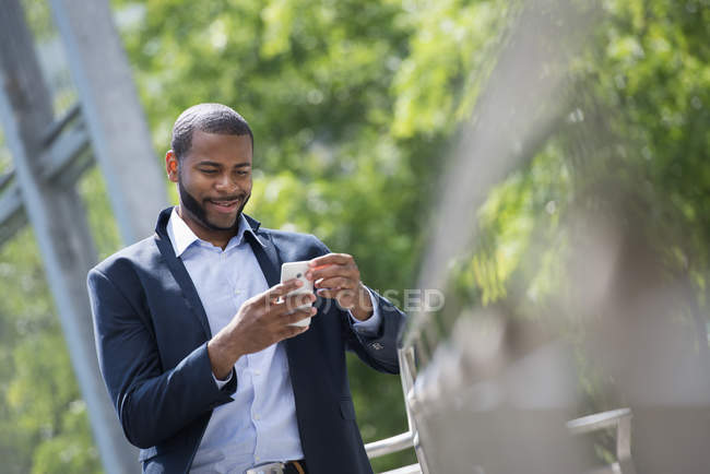 Бізнесмен в синій куртці, використовуючи смартфон на міській вулиці . — стокове фото