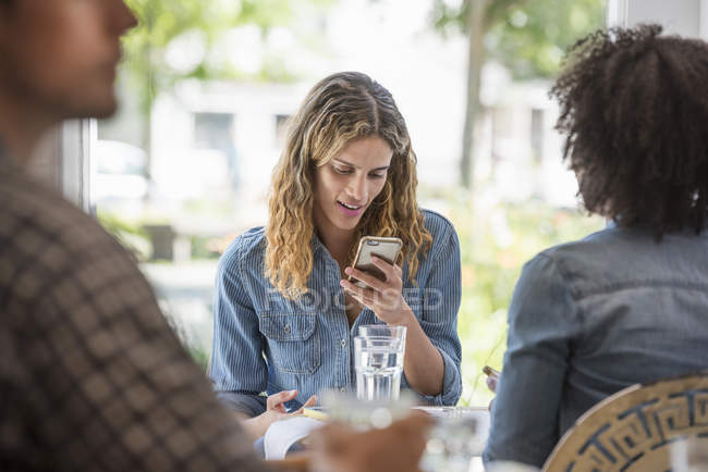 Woman checking smartphone while sitting with friend in coffee shop interior. — Stock Photo