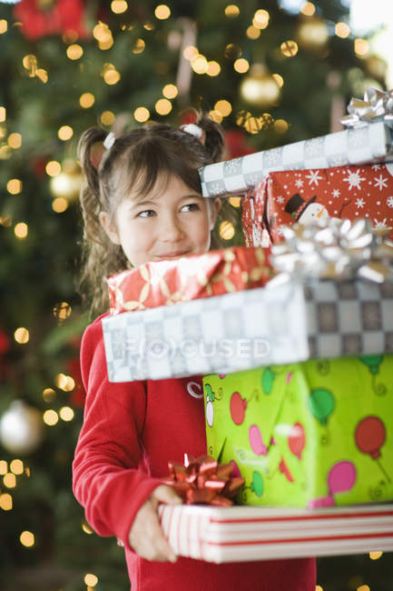 Mädchen im Grundalter trägt Stapel von Weihnachtsgeschenken. — Stockfoto