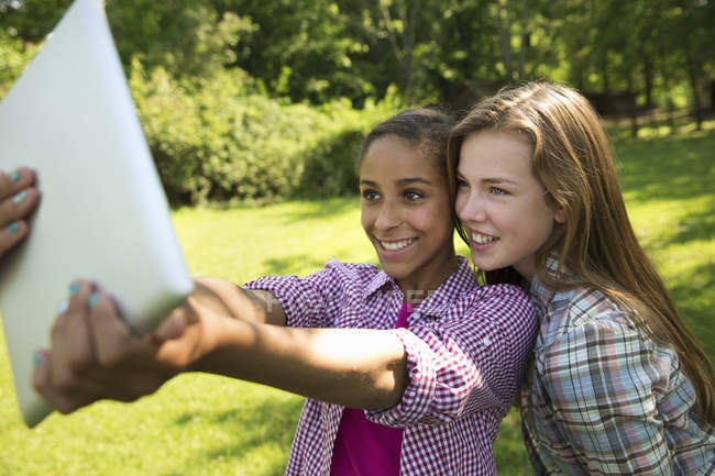 Duas meninas usando tablet digital e tomando selfie ao ar livre . — Fotografia de Stock