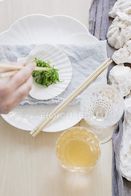 Vista de ángulo alto de la mano femenina usando palillos para ensalada de algas marinas . - foto de stock
