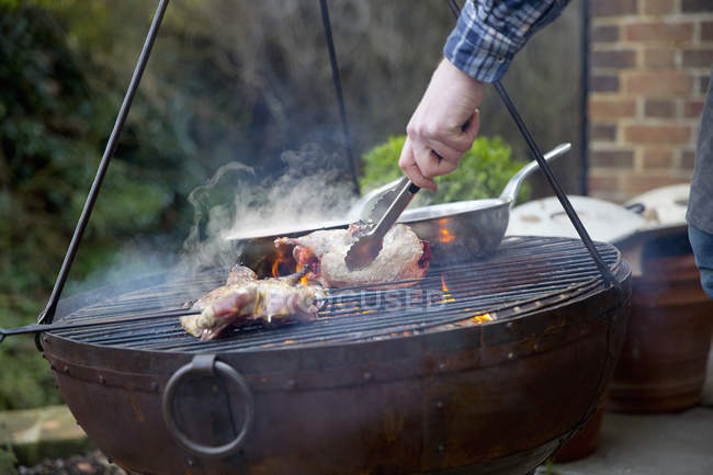 Close-up of man using tongs while roasting bird pieces on barbecue. — Stock Photo