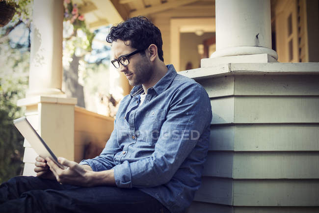 Человек с цифровым планшетом на крыльце в загородном доме . — стоковое фото