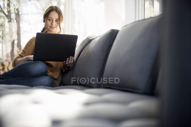 Donna seduta sul divano e con in mano un computer portatile . — Foto stock
