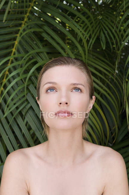 Jeune femme aux épaules nues regardant vers le haut avec des plantes tropicales en arrière-plan . — Photo de stock