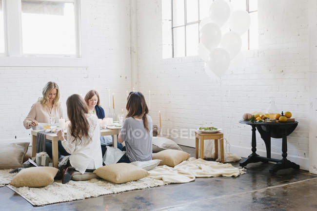 Vier Frauen sitzen an einem niedrigen Tisch auf Kissen und essen. — Stockfoto